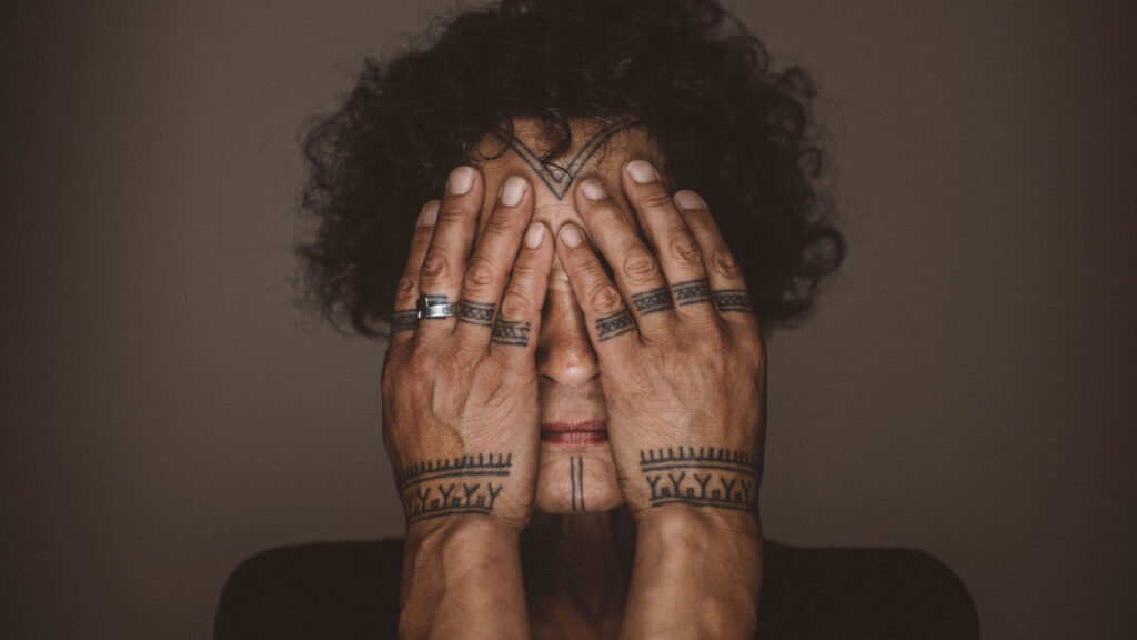 indigenous person holding their hands in front of their face