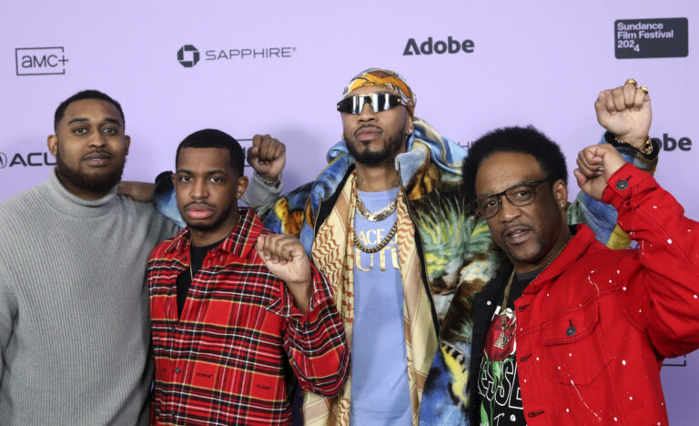 Four men stand side by side, each with a fist raised, in front of a 2024 Sundance Film Festival backdrop.