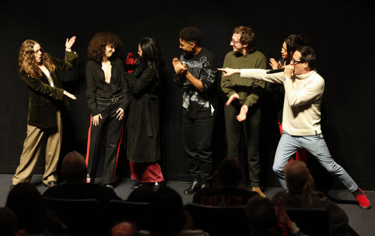 In a white sweater, Greg Jardin enthusiastically introduces his cast.