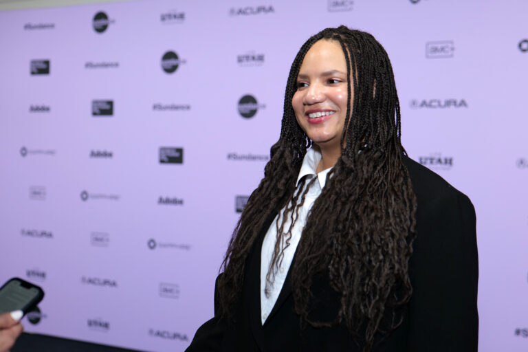 Haley Elizabeth Anderson stands in front of a white 2024 Sundance Film Festival backdrop. She is wearing a black blazer.